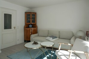 A living room with a sofa, two small tables, a cabinet, and a door. - Friesenring 17c - Cozy Vacation Rental at Friesenring 17c in Wenningstedt (Wenningstedt-Braderup (Sylt))
