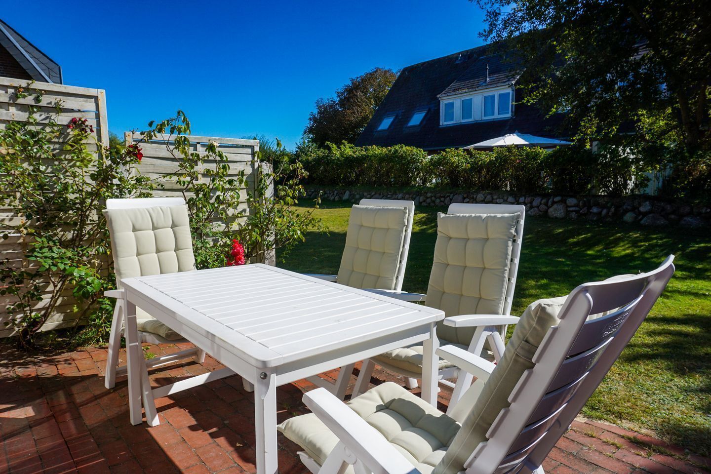 Une terrasse extérieure avec une table blanche et quatre chaises rembourrées.