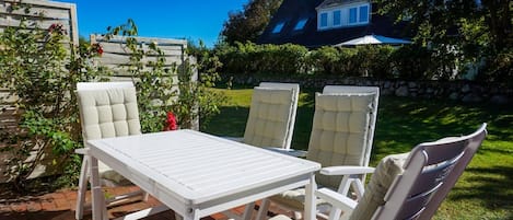 An outdoor patio with a white table and four cushioned chairs.
