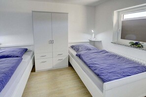 Ein Schlafzimmer mit zwei Einzelbetten, einem Kleiderschrank, einem Nachttisch mit Lampe und einem Fenster mit Jalousien.