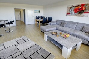 Ein modernes Wohnzimmer mit einem grauen Ecksofa, einem Couchtisch und einem Essbereich mit Tisch und Stühlen.