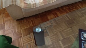 Un sofá color beige con una manta a rayas, un cesto de basura pequeño y un suelo de madera con diseño.