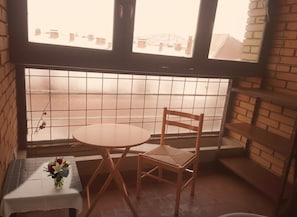 Ein Eckzimmer mit Fenster, einem kleinen Tisch mit Blumenvase und einem Holzstuhl.