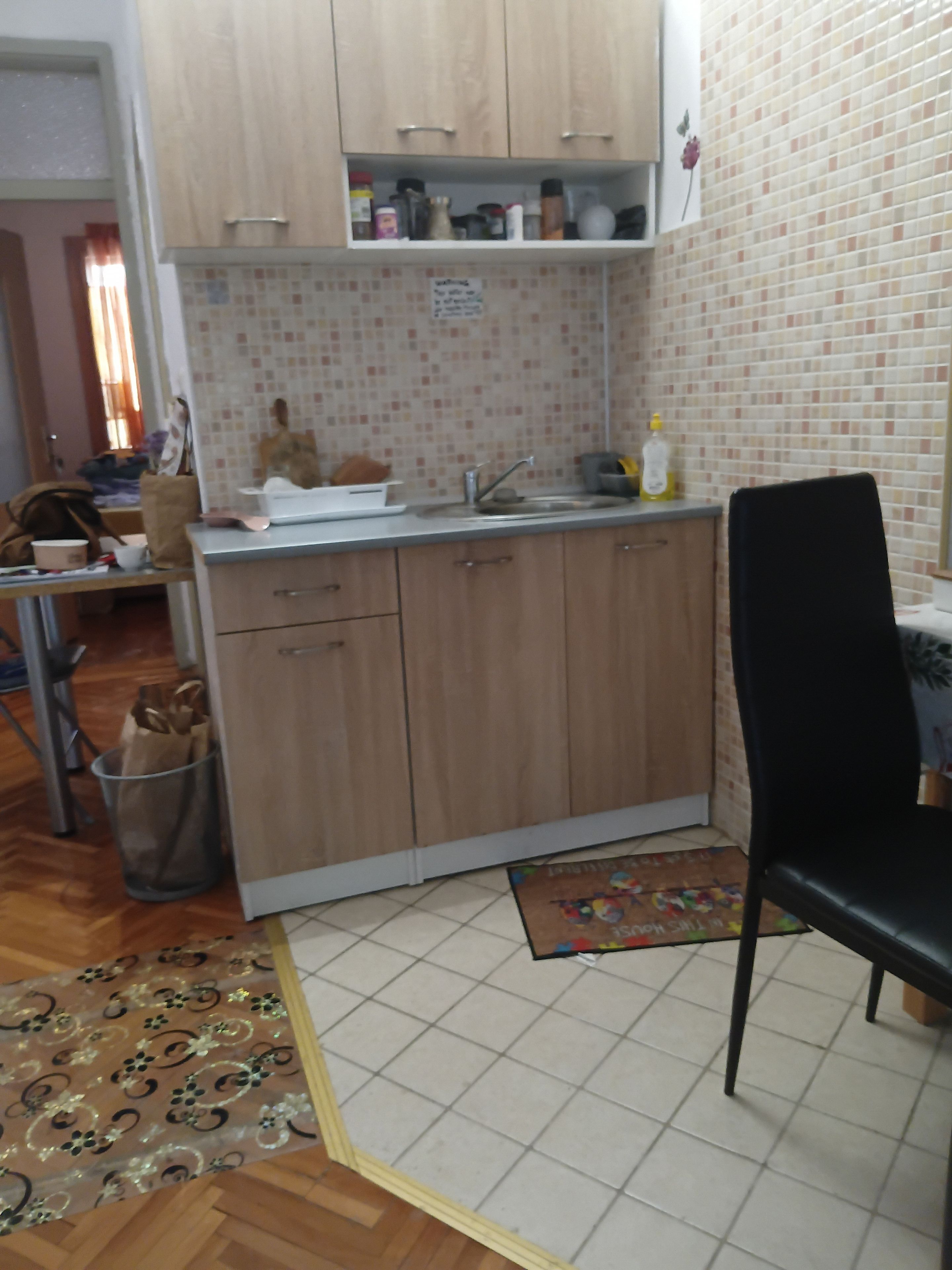 Cozinha compacta com armários de madeira, pia e área de jantar com uma cadeira preta.