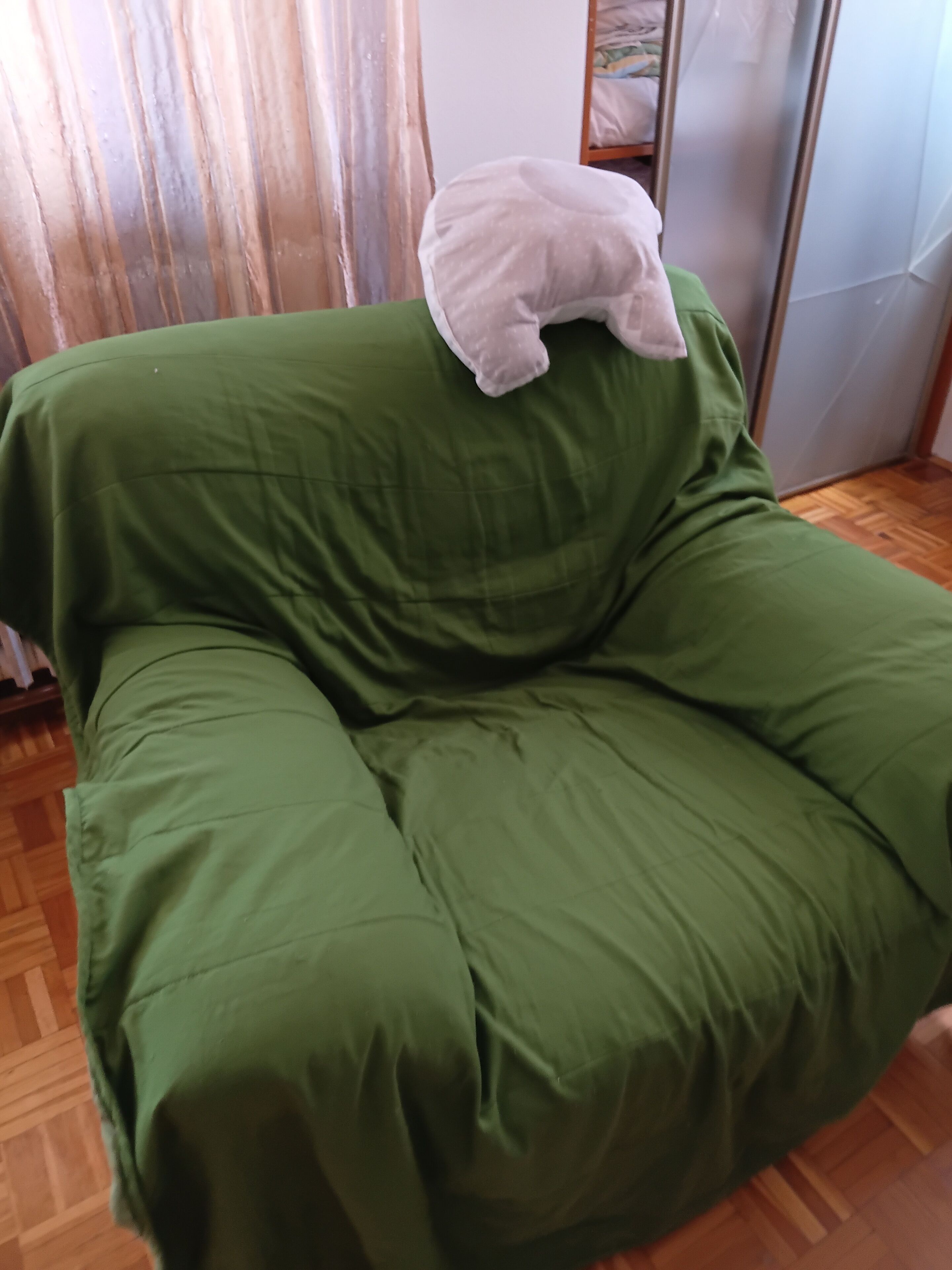 En grøn sofa med en hvid pude i et rum med trægulv og gardin.