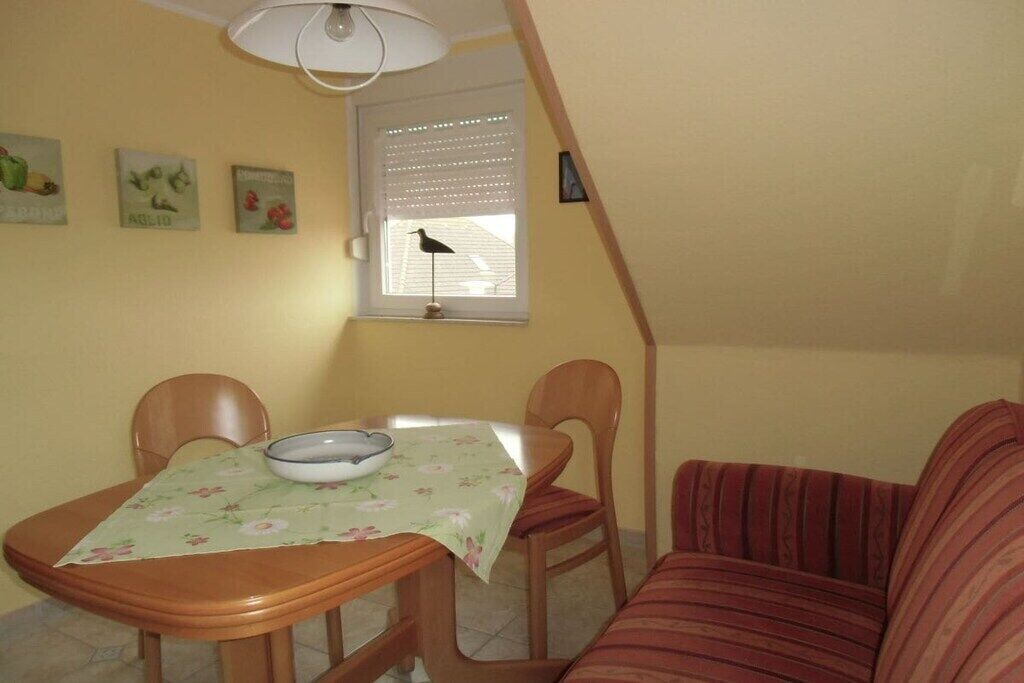 A dining area with a table and chairs, a window with blinds, and a wall with framed pictures.