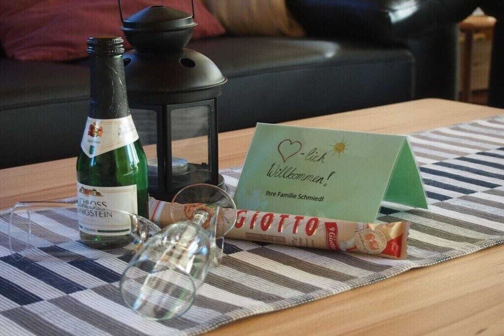 Una botella de vino, una copa, una vela, una tarjeta y una caja sobre un mantel a cuadros.