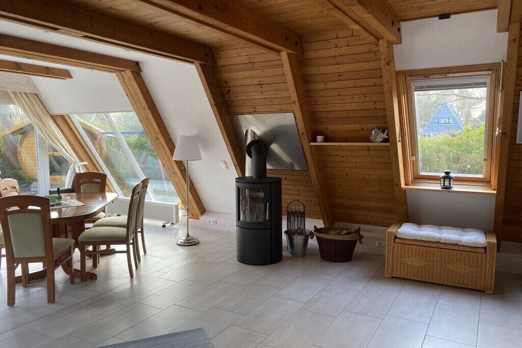 A cozy room with a wooden ceiling, a dining table with chairs, a black stove, and a wicker bench.