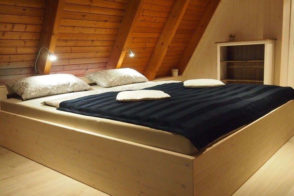 A wooden bed in a room with sloped ceilings and a built-in shelf.