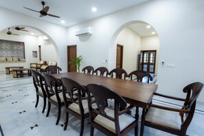 A dining area with a long wooden table, multiple chairs, and a ceiling fan. - Utamber House (Jodhpur)