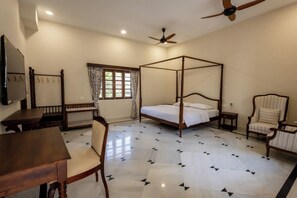 A four-poster bed with a wooden frame, a ceiling fan, a television on the wall, and a window with curtains. - Utamber House (Jodhpur)
