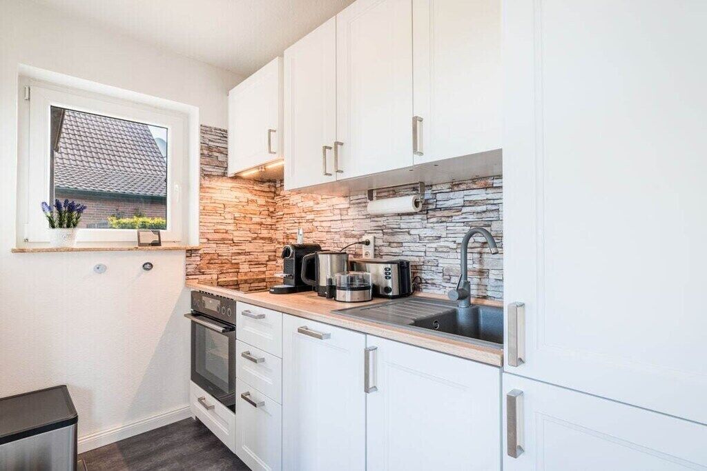 A compact kitchen with white cabinets, a stone backsplash, and modern appliances.