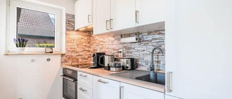 A compact kitchen with white cabinets, a stone backsplash, and modern appliances.