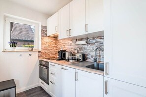 A compact kitchen with white cabinets, a stone backsplash, and modern appliances. - Holiday home starboard (Wittmund OT Carolinensiel)