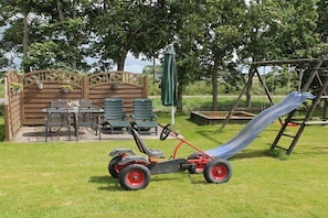 A children's play area with a slide, a swing set, and a seating area with tables and chairs. - Holiday apartment with 2 bedrooms (Midlum)
