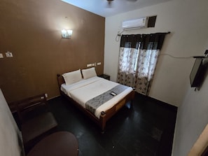 Un lit simple avec une tête de lit, une table de chevet, une chaise, un appareil de climatisation et une fenêtre avec des rideaux.