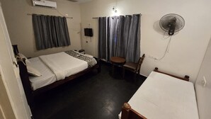 A hotel room with a bed, a desk, a chair, a fan, an air conditioner, and curtains. - Grace Residency (MADURAI)