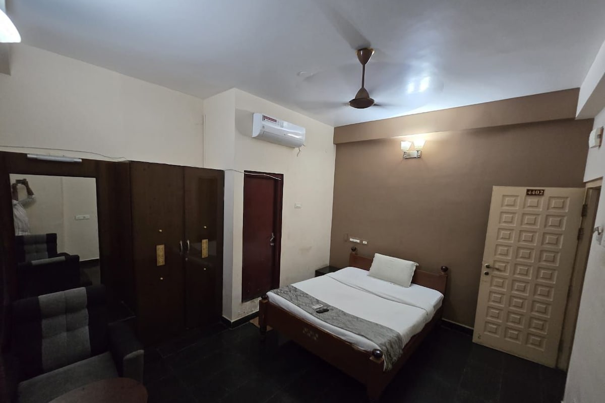 Une chambre d’hôtel avec un lit, un bureau, une chaise, une armoire et une porte.