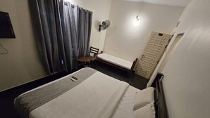 A hotel room with a bed, a chair, a small table, a fan, and a door. - Grace Residency (MADURAI)