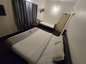 Une chambre d’hôtel avec un lit, une chaise, une petite table, un ventilateur et une porte.