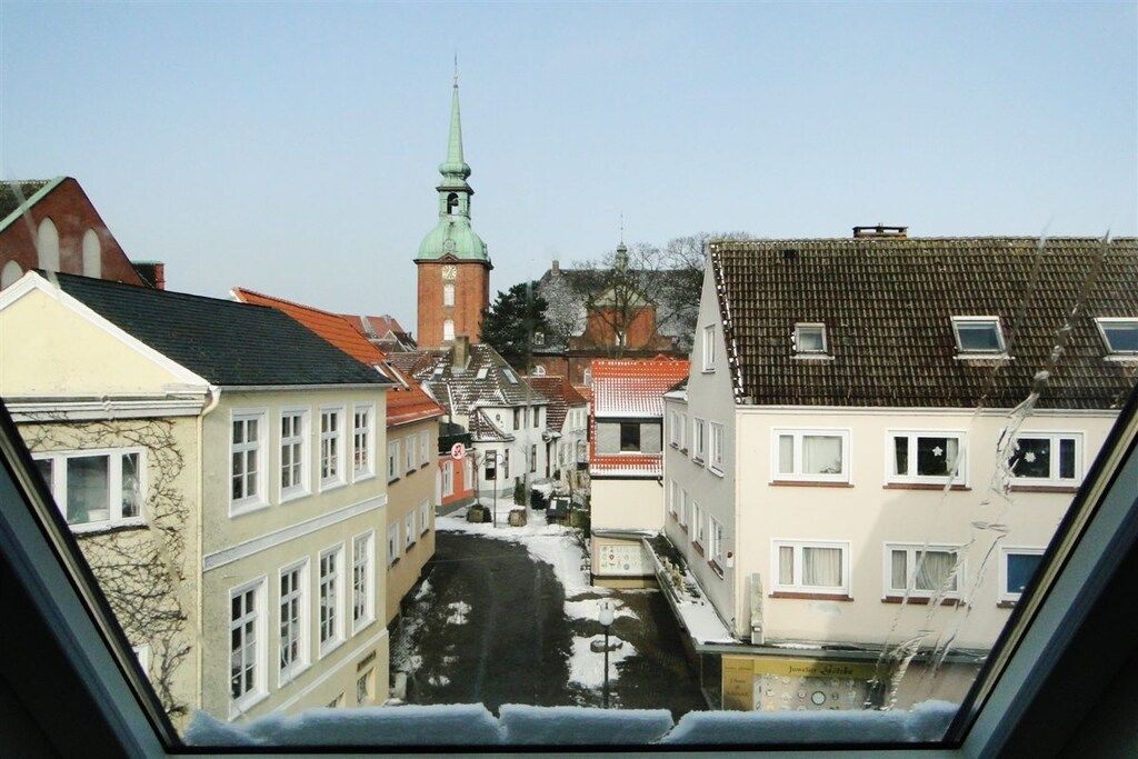 A narrow street with buildings on either side, a church with a green spire, and a clear sky.