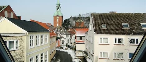 En smal gade med bygninger langs begge sider, en kirke med et grønt spiret tårn, og en klar himmel.