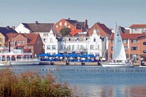 A waterfront scene with buildings, a sailboat, and a riverboat. - Holiday apartment with 1 bedroom (Kappeln Stadt)