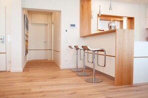 A modern kitchen with wooden flooring, a built-in bar area with three stools, and a white refrigerator. - Holiday apartment with 1 bedroom (Kappeln Stadt)