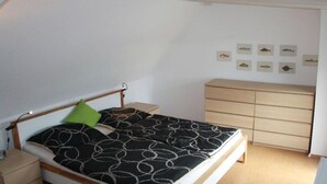 A bedroom with a bed, a bedside table, a dresser, and wall-mounted fish decorations. - Holiday home Seestern (Hasselberg)