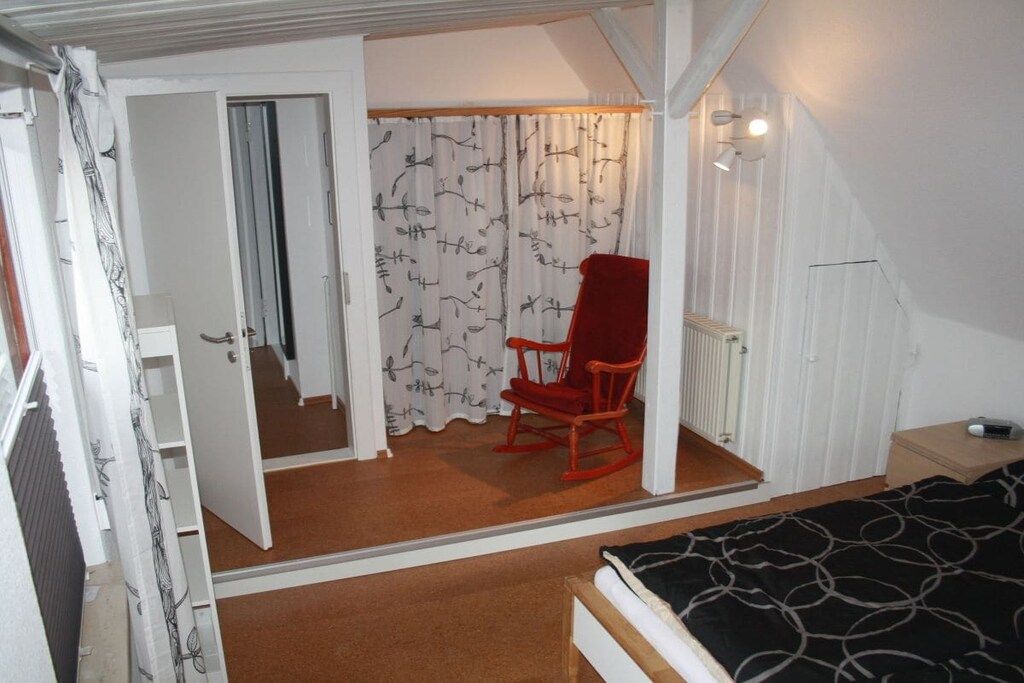A bedroom with a bed, a red rocking chair, a window with curtains, and a radiator.