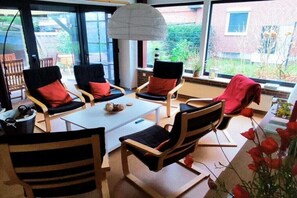 A room with a large window, two chairs with red cushions, a white table, and a hanging light fixture. - Holiday home Seestern (Hasselberg)