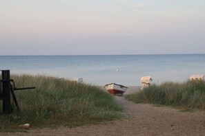Caminho de praia que leva ao mar, com um barco e um buggy.