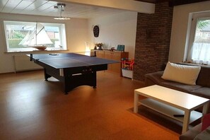 A room with a ping pong table, a sofa, a coffee table, a brick wall, and a window with a sailboat view. - Holiday home Seestern (Hasselberg)