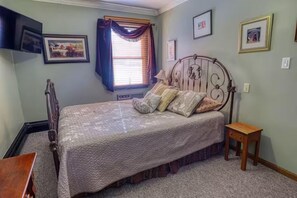 Un dormitorio con cama, mesita de noche, ventana con cortinas y una obra de arte colgada en la pared.