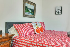 A bedroom with a bed, a wooden nightstand, a framed landscape painting, and a framed abstract art piece.