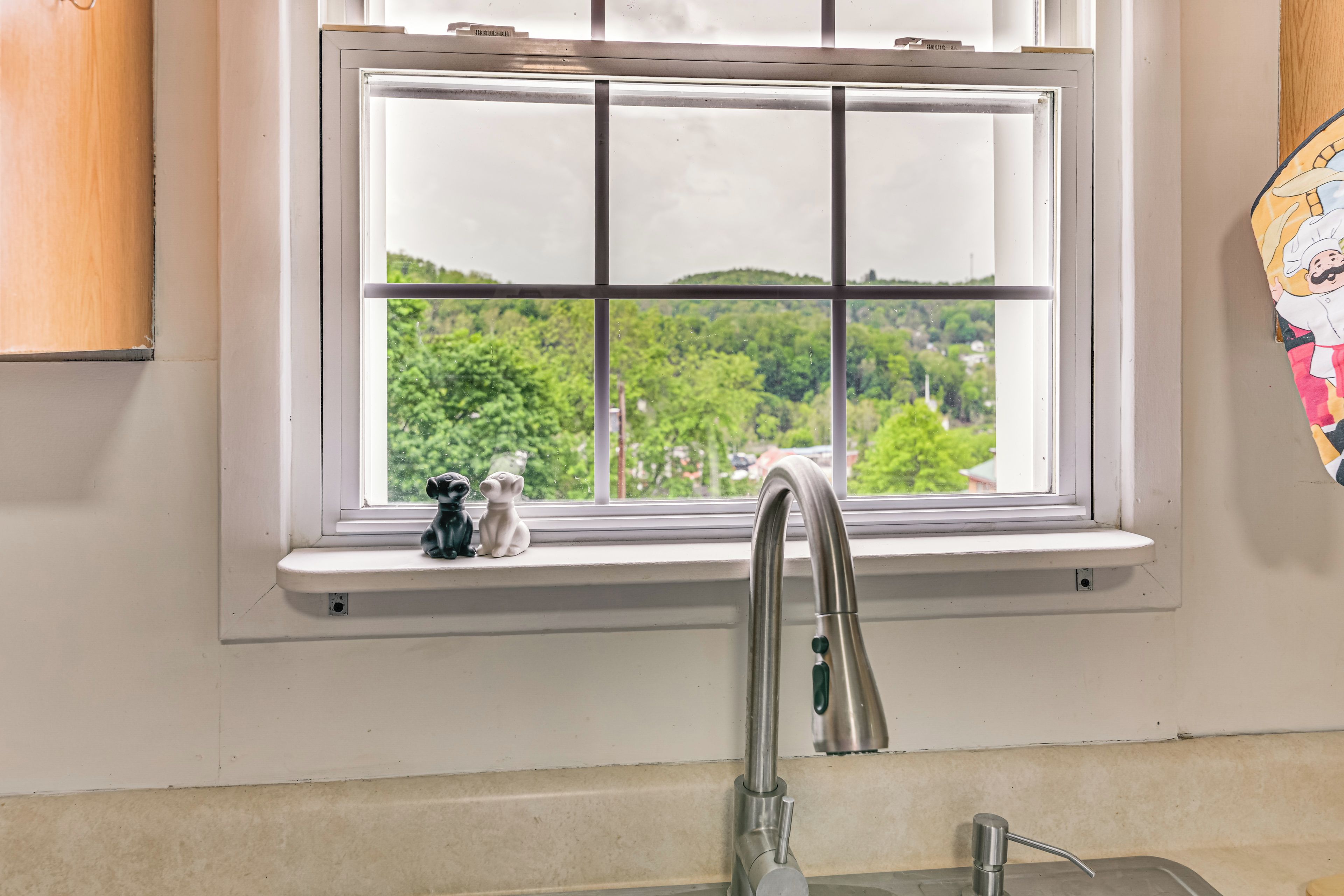 A kitchen with a window, a stainless steel faucet, and a small shelf with two ceramic figurines.