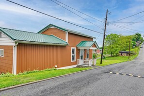 A two-story wooden house with a green roof, a front porch, and a driveway.