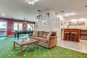 Ein Wohnzimmer mit Billardtisch, einem gemusterten Sofa und einem grünen Teppich mit Rasteroptik.