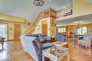 A spacious living area with a large sectional sofa, a dining table with chairs, and a staircase with wooden railings. - Hot Tub Ski Home: Rooster's Den in Ellicottville (Ellicottville)