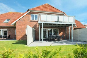 A two-story house with a covered patio area, a brick exterior, and a tiled roof. - Holiday apartment with 2 bedrooms (Carolinensiel)