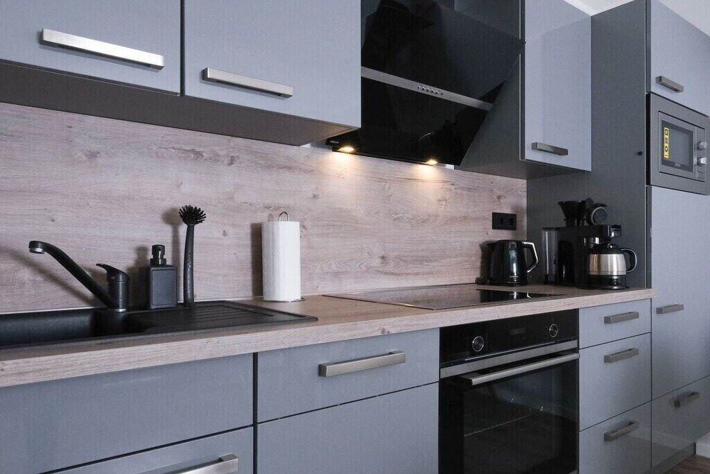 Une cuisine moderne avec des meubles de couleur grise, un plan de travail en bois, une hotte noire et une machine à café.
