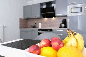 Una cocina con electrodomésticos modernos, una mesa de comedor con un frutero que contiene manzanas y plátanos.