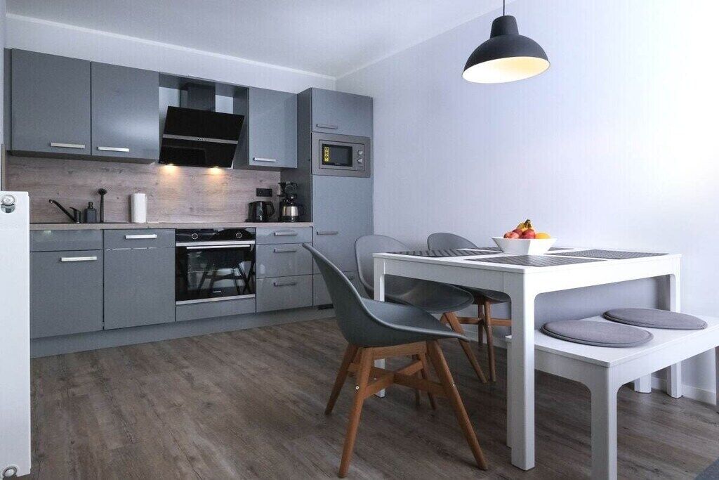 Cuina moderna amb armaris grisos, taula de dinar blanca i llum penjant.