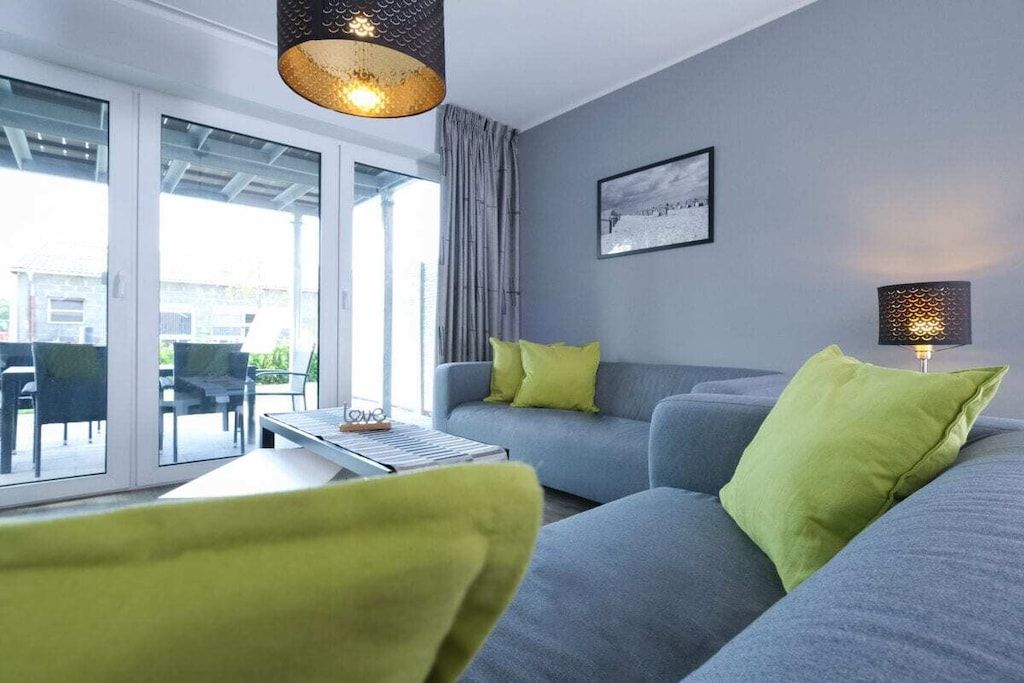 Un salon moderne avec un canapé gris, des coussins verts, une table basse et un luminaire suspendu.