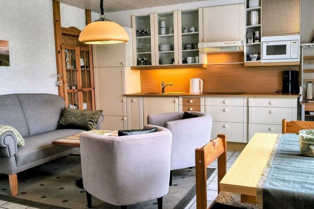 Un salon moderne comprenant un canapé, des fauteuils, une table basse et une table à manger. Il y a également un coin cuisine avec des placards, un four à micro-ondes et une machine à café.