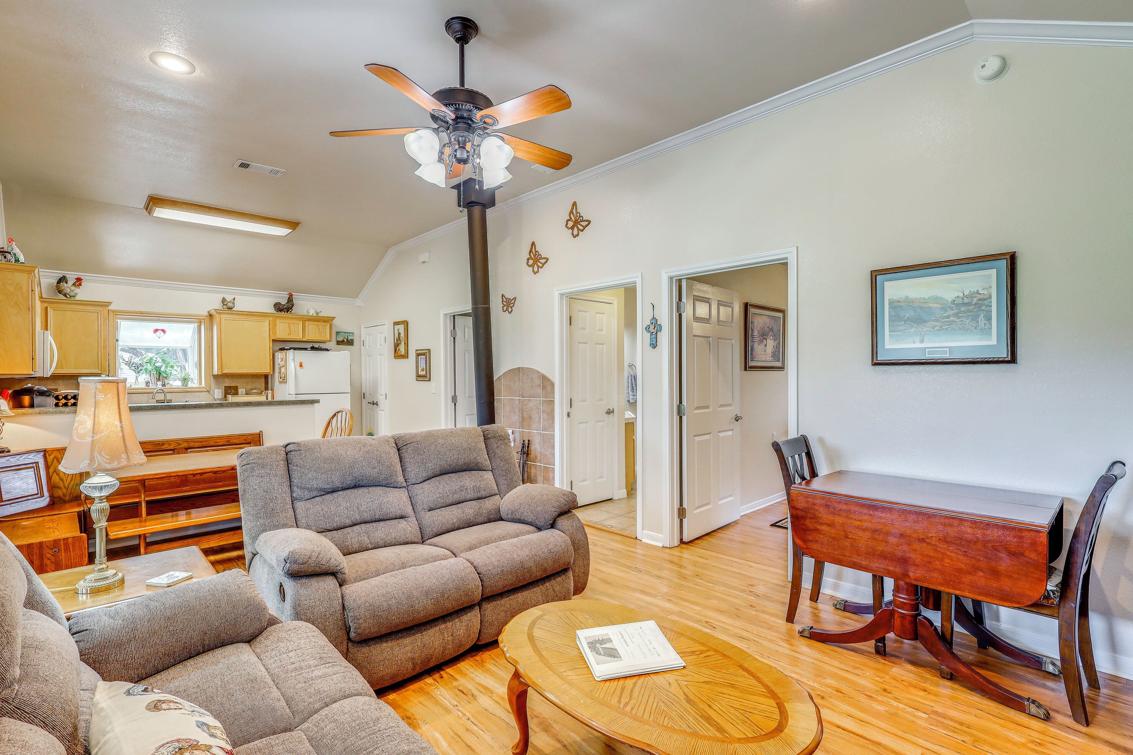 A spacious living room with a ceiling fan, a dining table with chairs, and a kitchen area in the background.