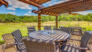 Une terrasse extérieure avec une table ronde et des chaises en osier, entourée d’une pergola en bois.