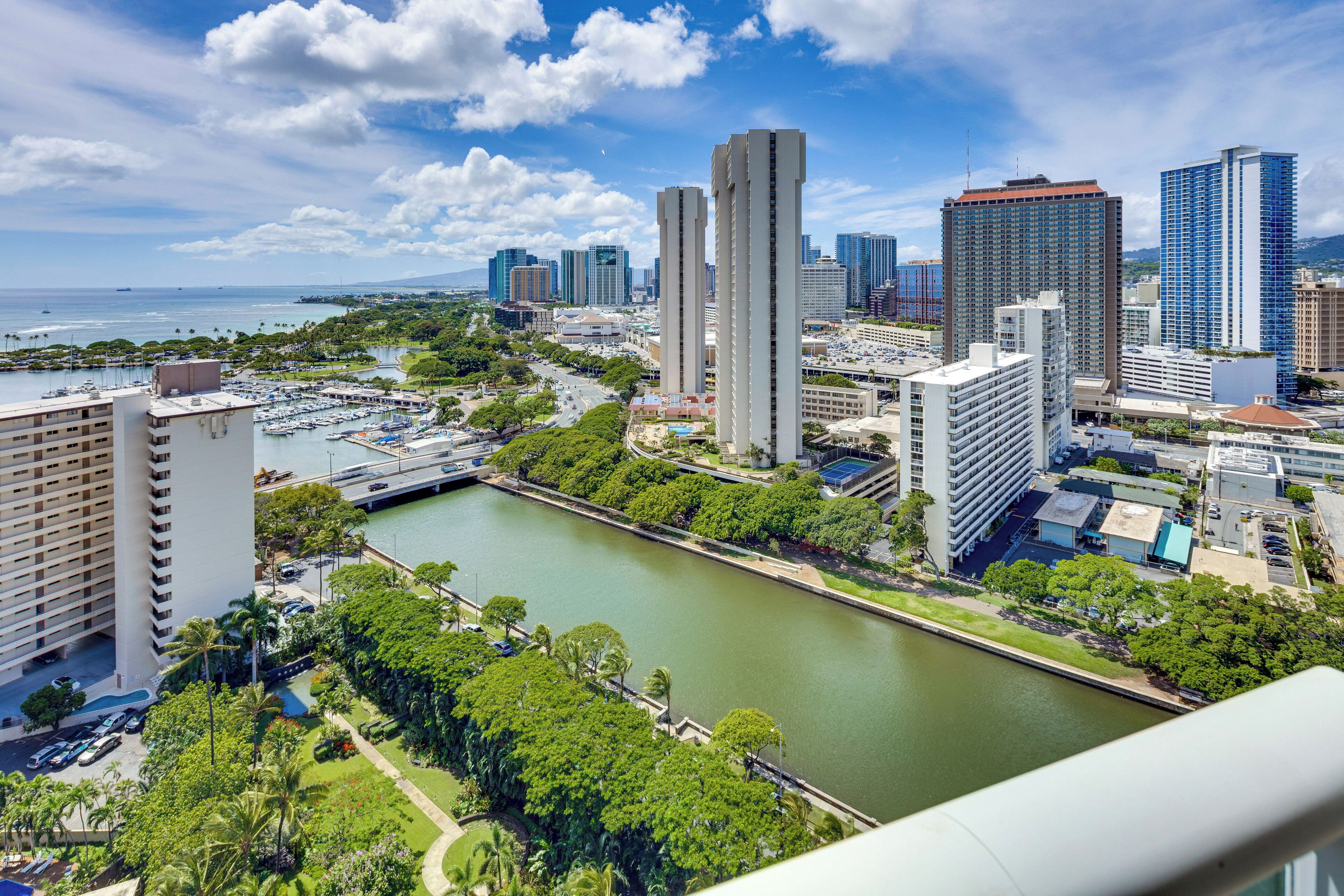Un paisaje urbano con un río, rascacielos y un puerto deportivo.