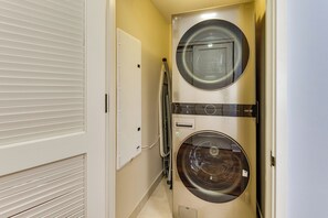 A compact laundry room with two stacked washers and dryers, a white door, and a tiled floor. - Walk to Beach, Shopping & Dining! Waikiki-Area (Honolulu)