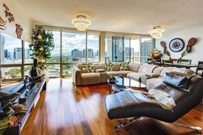 A spacious living room with a large window, a sofa, a coffee table, and a leather armchair. - Walk to Beach, Shopping & Dining! Waikiki-Area (Honolulu)